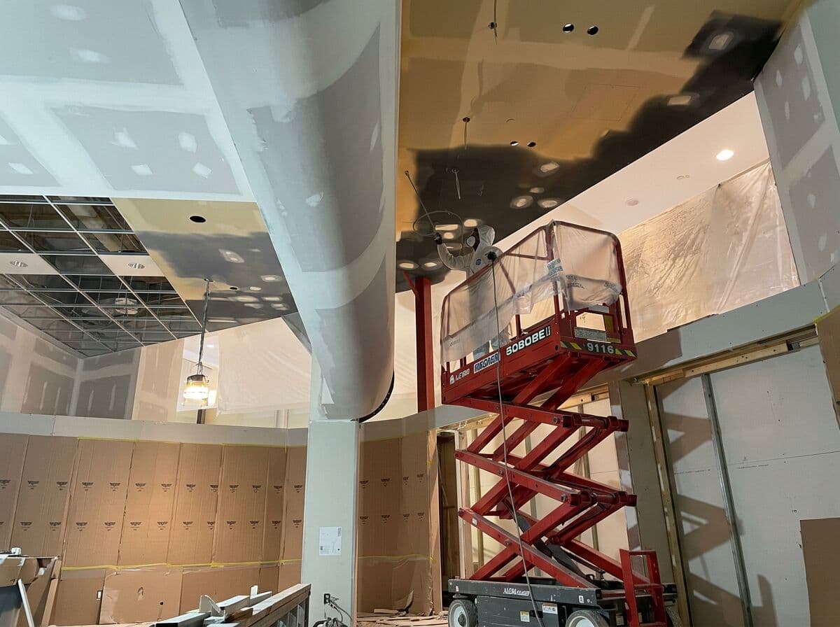 Ceiling spray paint in progress at YOMG — scissor lift and protective sheeting set up by VD Painting (work in progress)