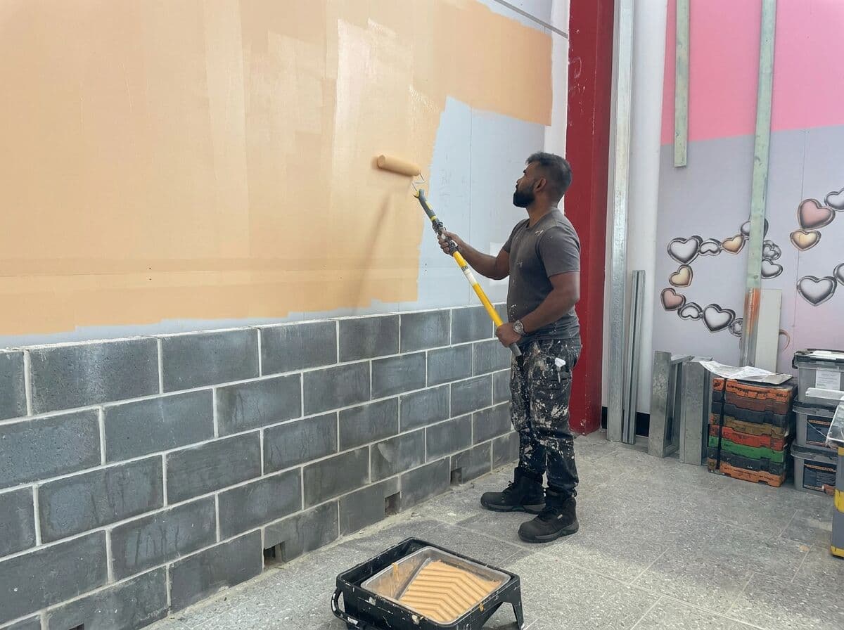 VD Painting crew member rolling paint onto the external wall of YOMG with an extension roller (work in progress)