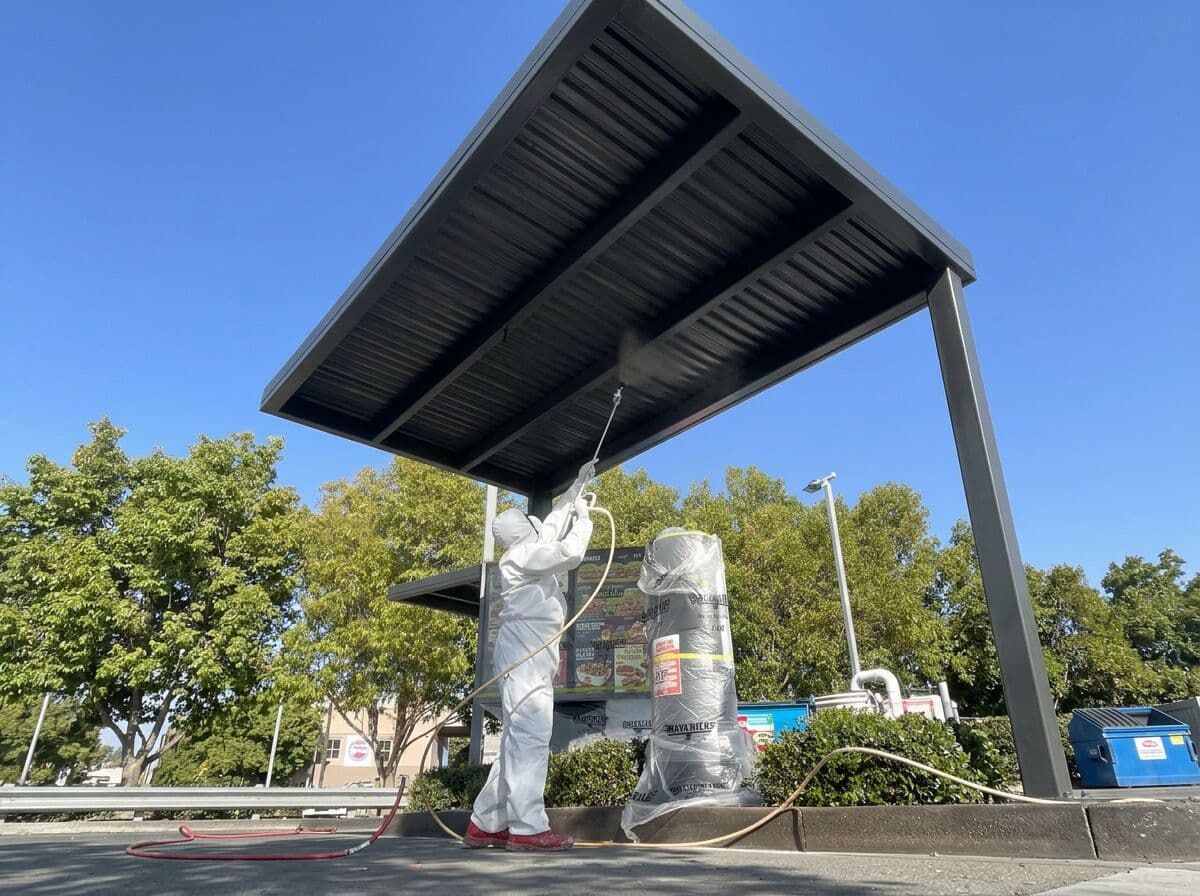 VD Painting crew member in full protective suit spray painting the underside of the Hungry Jack's drive-thru canopy roof
